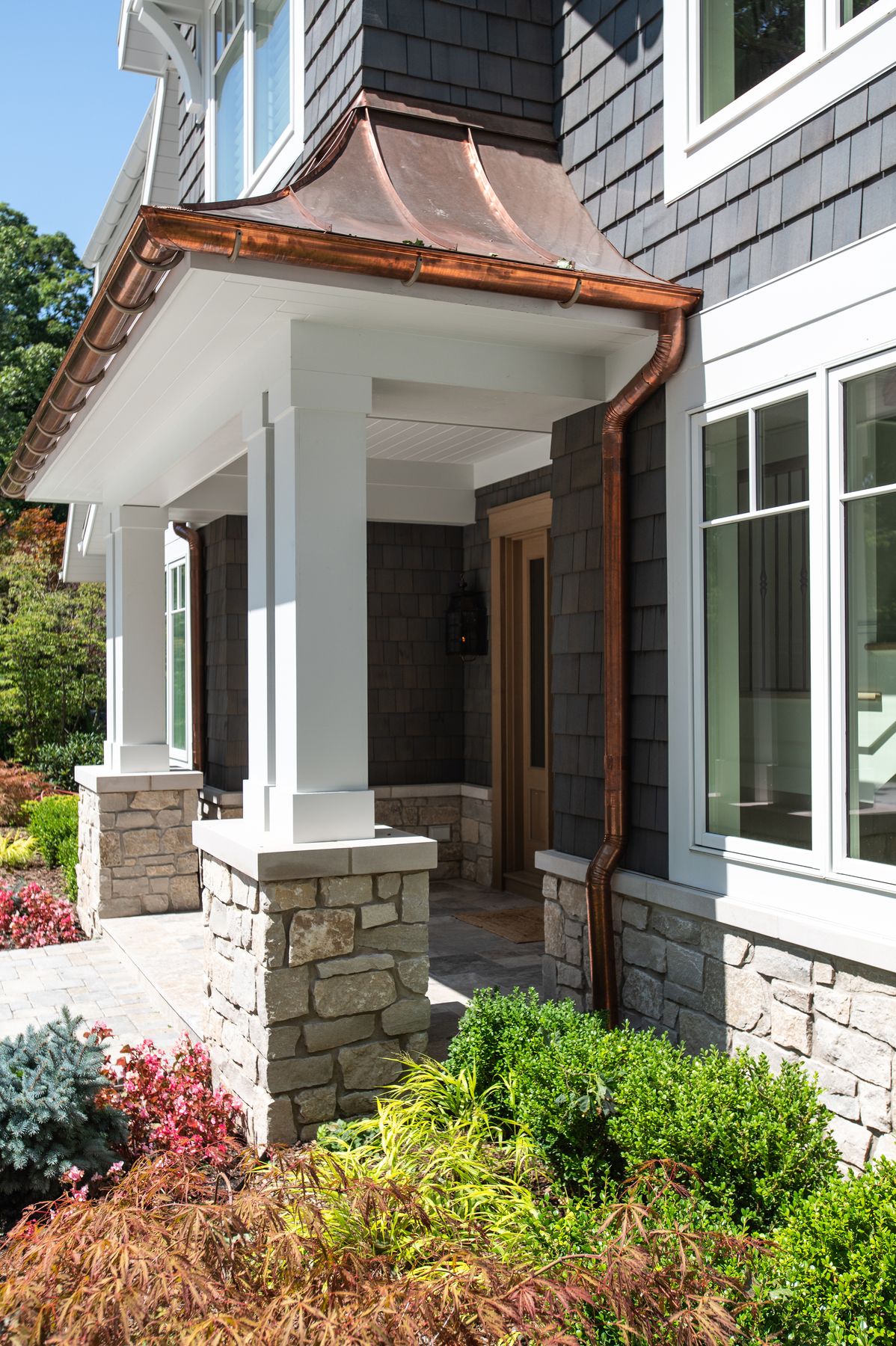 Black River Ashlar stone piers and wainscot beneath a copper-roofed portico by Mike Schaap Builders